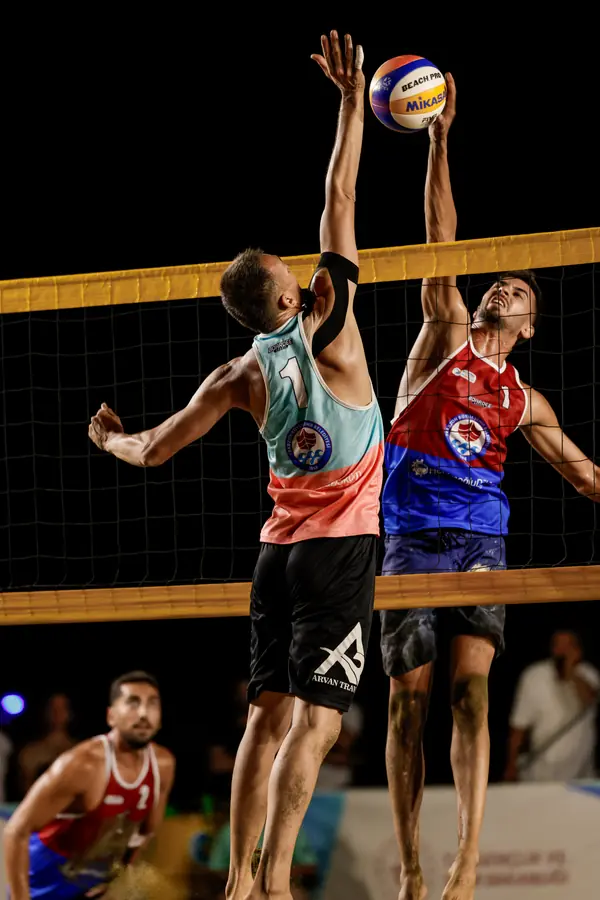 Two players contest the ball above the net under night lights